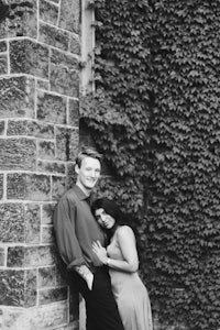 a black and white photo of a couple leaning against a wall